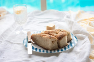 Focaccia Bread on a plate with butter and knife and drink and pool in background