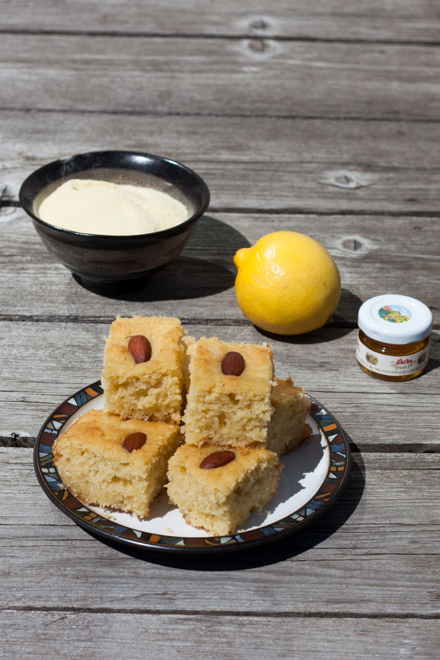egyptian basbousa cake with a bowl of semolina, a lemon and a jar of honey on a wooden table