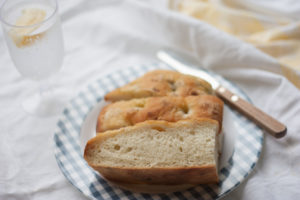 Focaccia Bread with sea salt and black pepper on a plate with butter knife and drink