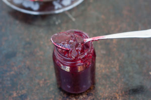 red gooseberry elderflower jam in a jar with a spoon