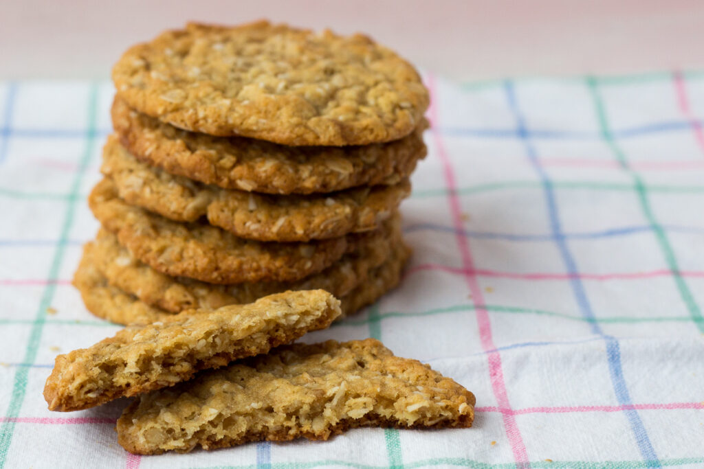 stack of orange maple anzac cookies with one broken in half