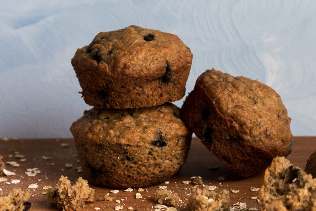 three blueberry banana muffins stacked on cutting board