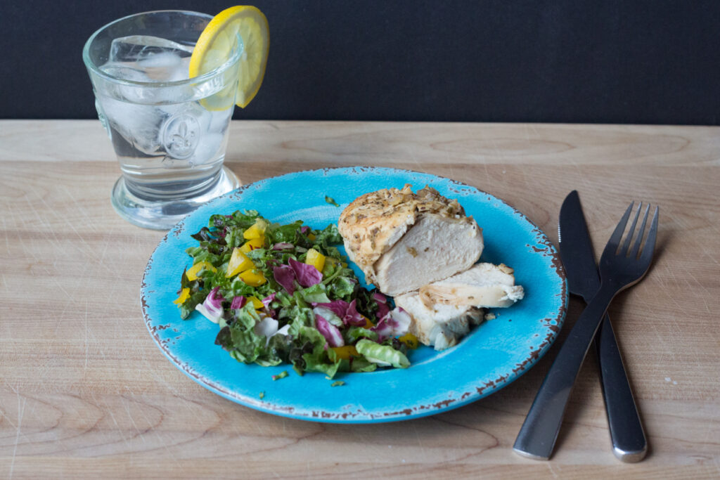 chicken and salad on a blue plate with a glass of water